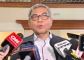 Seorang pria berkacamata dengan rambut beruban berbicara di hadapan sejumlah mikrofon wartawan