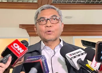 Seorang pria berkacamata dengan rambut beruban berbicara di hadapan sejumlah mikrofon wartawan