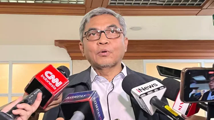 Seorang pria berkacamata dengan rambut beruban berbicara di hadapan sejumlah mikrofon wartawan