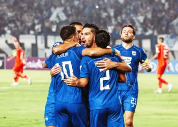 Beberapa pemain Persib Bandung berseragam biru saling berpelukan saat merayakan gol di lapangan, dengan pemain lawan berbaju oranye di belakang