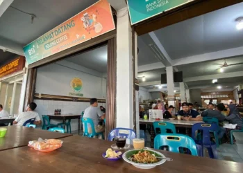 Suasana warung kopi Solong Coffee Ulee Kareng dengan pengunjung yang duduk di meja, serta minuman kopi dan hidangan di bagian depan.