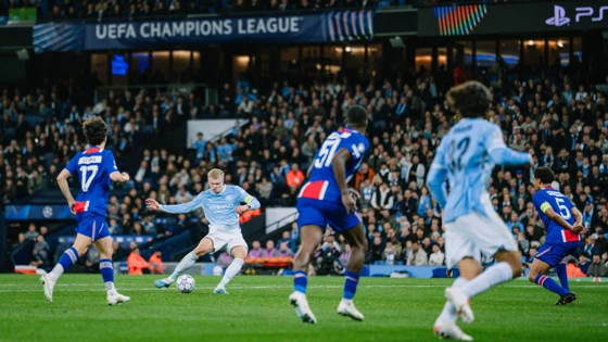 Pemain Manchester City berseragam biru muda melepaskan tembakan di antara pemain Paris Saint-Germain berseragam biru tua di lapangan
