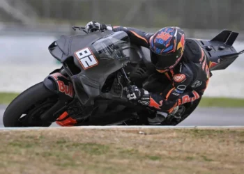 Motor balap prototipe KTM hitam bernomor 86 melaju miring di tikungan sirkuit, dengan pengendara memakai helm dan pakaian balap