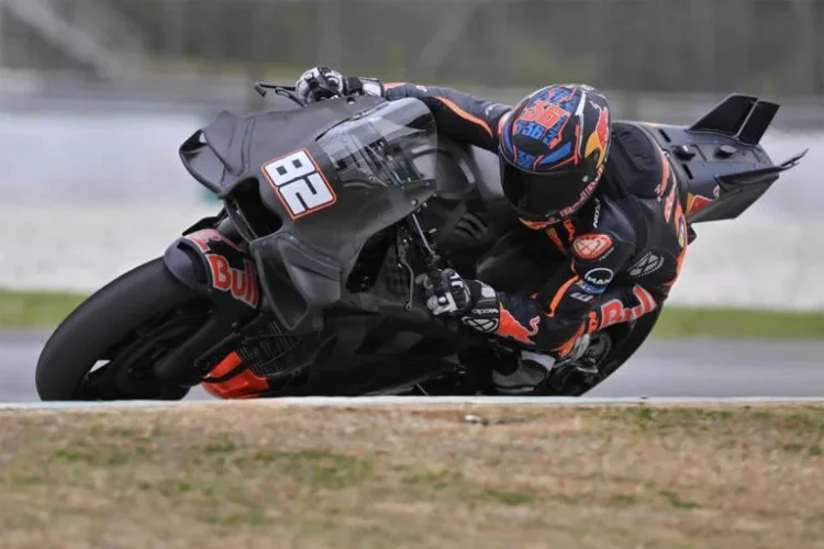 Motor balap prototipe KTM hitam bernomor 86 melaju miring di tikungan sirkuit, dengan pengendara memakai helm dan pakaian balap