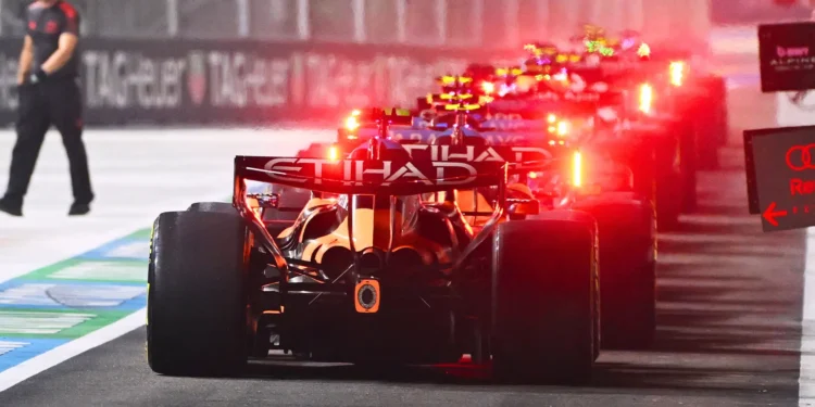 Tampak belakang sejumlah mobil Formula 1 berjajar di jalur pit dengan lampu merah menyala
