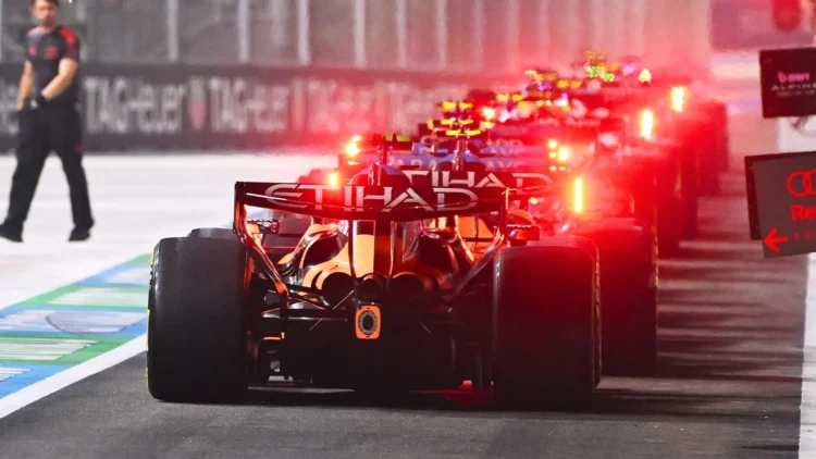 Tampak belakang sejumlah mobil Formula 1 berjajar di jalur pit dengan lampu merah menyala