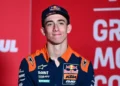 Pembalap Red Bull KTM mengenakan topi biru tua dan kemeja tim oranye-biru dengan latar merah