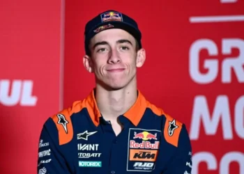 Pembalap Red Bull KTM mengenakan topi biru tua dan kemeja tim oranye-biru dengan latar merah