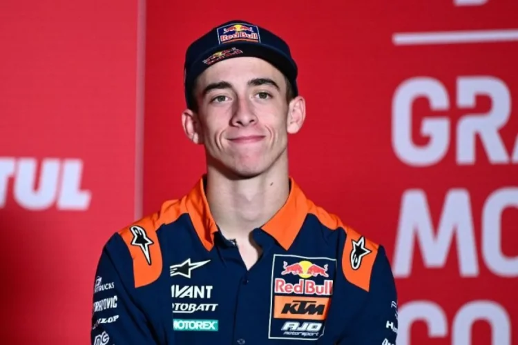 Pembalap Red Bull KTM mengenakan topi biru tua dan kemeja tim oranye-biru dengan latar merah
