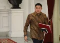 Seskab Teddy Indra Wijaya mengenakan kemeja batik dan membawa map merah saat berjalan di dalam gedung