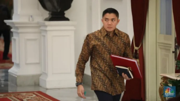 Seskab Teddy Indra Wijaya mengenakan kemeja batik dan membawa map merah saat berjalan di dalam gedung