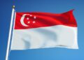 Bendera Singapura berwarna merah putih dengan bulan sabit dan lima bintang berkibar di langit biru