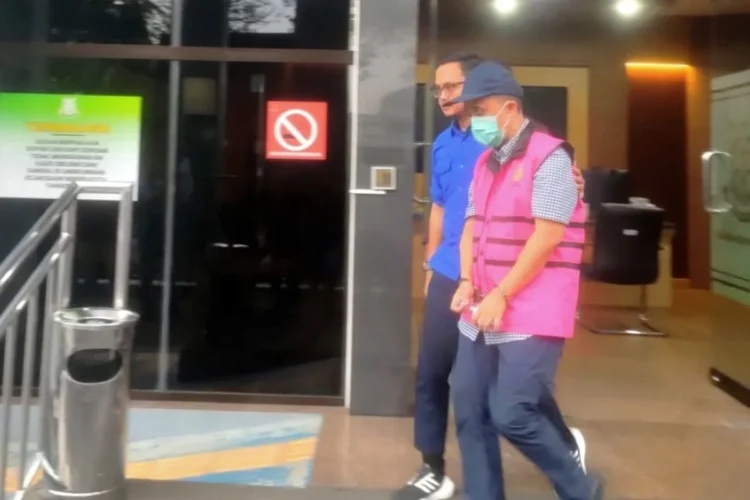 Pria mengenakan rompi tahanan merah muda dan masker berjalan didampingi petugas