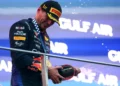 Max Verstappen mengenakan seragam Red Bull dan topi Pirelli sambil memegang botol sampanye di atas podium