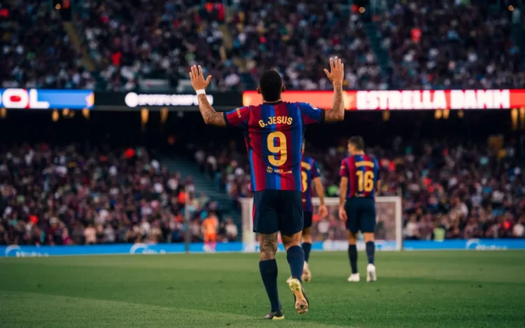 Pemain Barcelona bernomor punggung 9 dengan nama G. Jesus mengangkat kedua tangan di lapangan sepak bola