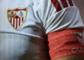 Detail lambang Sevilla FC pada bagian dada jersey putih serta ban kapten merah di lengan pemain.